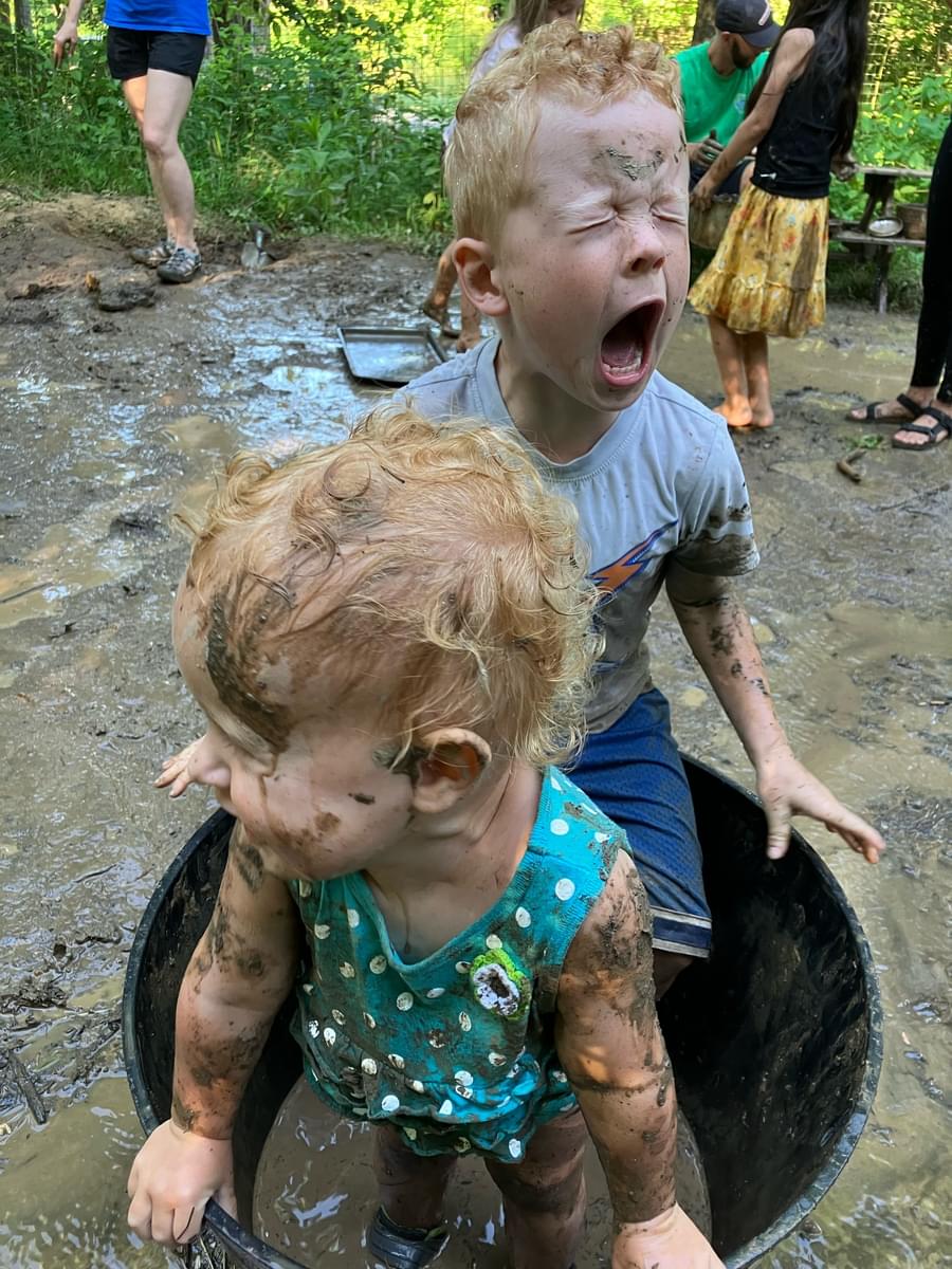 Two young boys in Nature PlayScape, one boy screaming with mud on face.